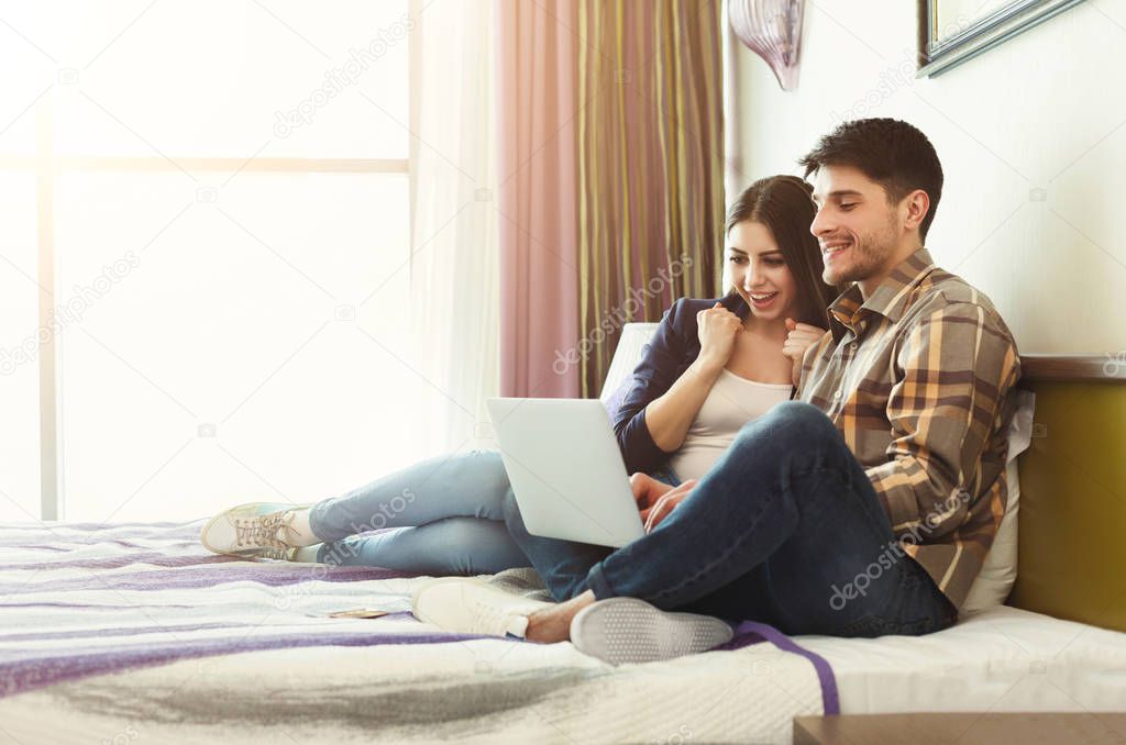 Happy couple using laptop in hotel room
