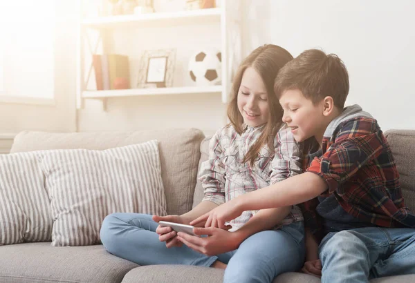 Deux enfants jouent sur le smartphone sur le canapé à la maison — Photo