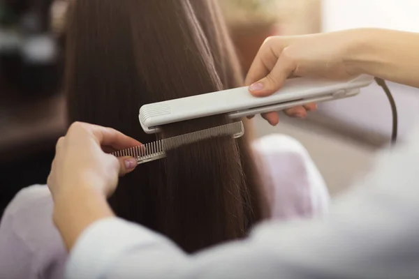 Парикмахер выпрямляет длинные каштановые волосы — стоковое фото