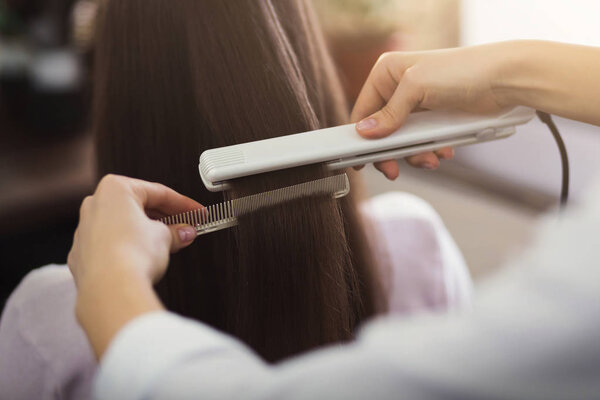 Парикмахер выпрямляет длинные каштановые волосы
