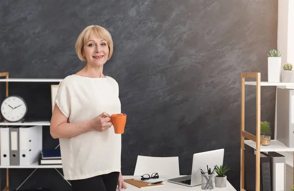 Sonriente mujer de negocios madura con taza de café en la oficina — Foto de Stock