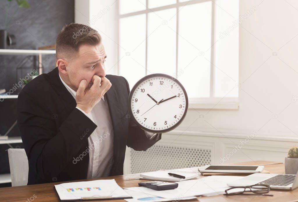 Worried businessman holding clock and looking at it
