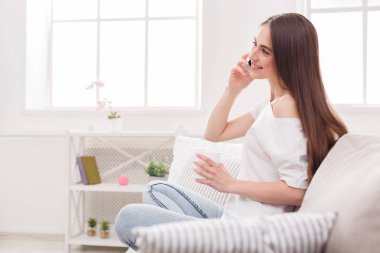 Cep telefonu ve kahve ile kanepede oturan genç kadın