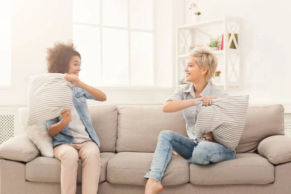 Две девушки дерутся подушками на диване — стоковое фото