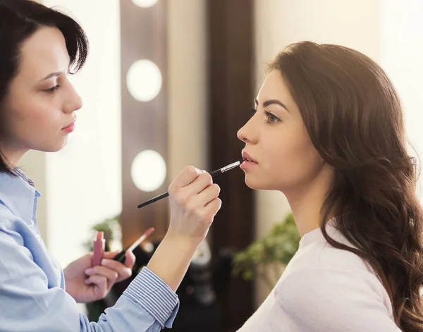 Maquiagem artista aplicando brilho em lábios de mulher no salão — Fotografia de Stock