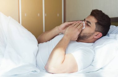 Hapşırma ve burun ile yatakta yatarken doku kapsayan genç adam