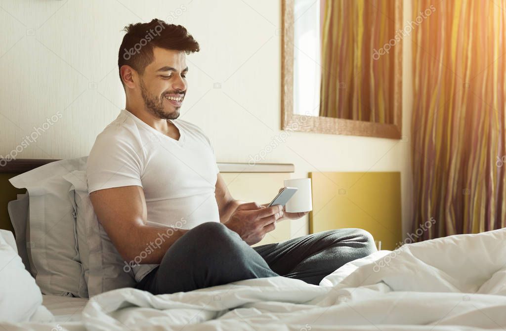 Young man sending message while sitting in bed