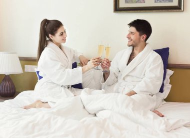 Romantic couple in bathrobes drinking champagne in bed clipart