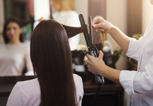 Hairdresser using curling iron at beauty salon
