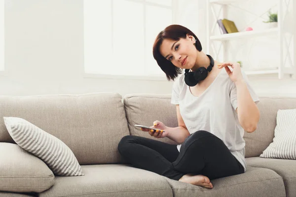Junge Frau mit Kopfhörern auf beigem Sofa — Stockfoto