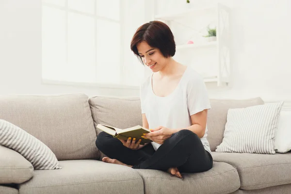 Молода брюнетка читає книгу на дивані — стокове фото