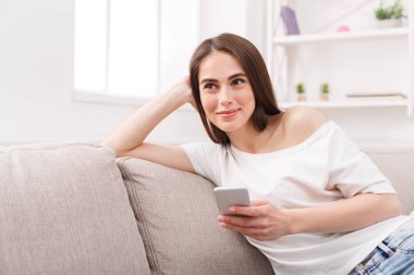 Cep telefonu ile kanepede oturan gülümseyen genç kadın