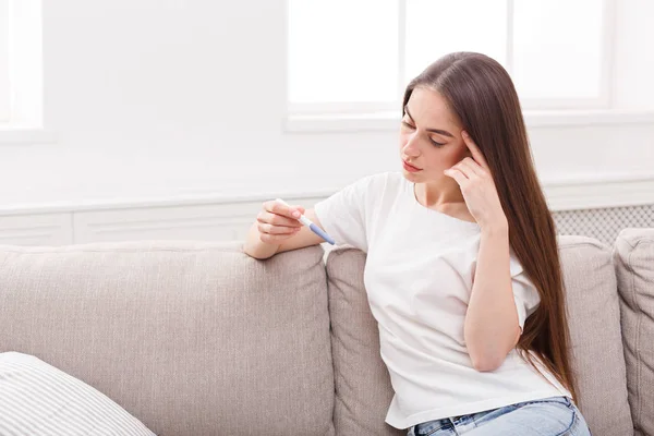 Worried girl with pregnancy test sitting on sofa — Stock Photo, Image