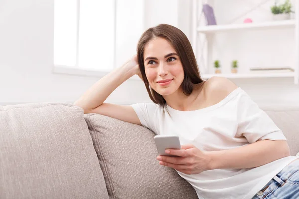 Lächelnde junge Frau sitzt mit Handy auf Sofa — Stockfoto