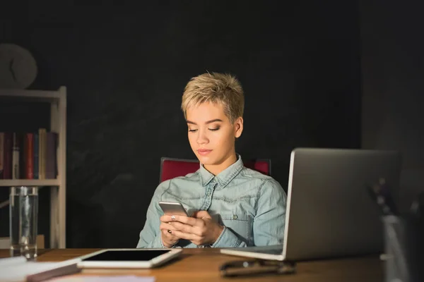 Frau schreibt SMS auf Smartphone, während sie im Home Office arbeitet — Stockfoto