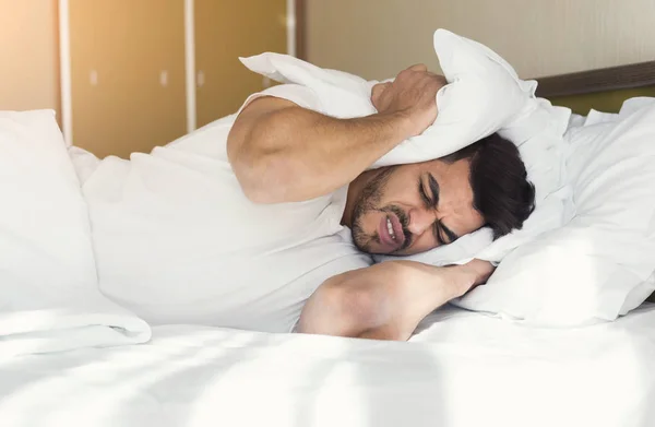 Młody człowiek próbuje spać krycia uszy z poduszką — Zdjęcie stockowe