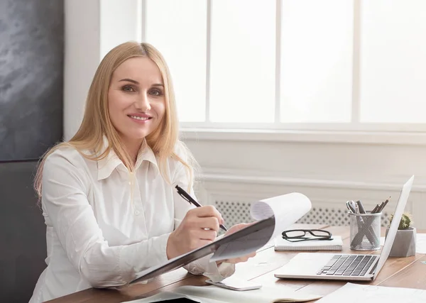 Ung succesfuld kvinde skriver noter, mens du sidder i kontoret - Stock-foto