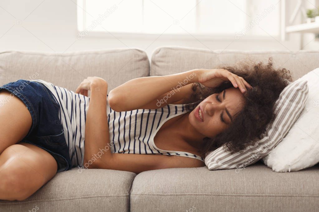 Sad black girl feeling pain lying on sofa