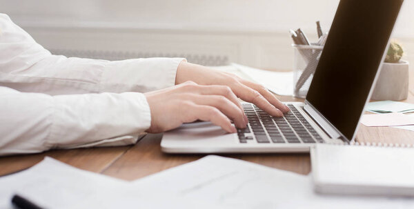 Side view of womans hands typing on laptop keyboard
