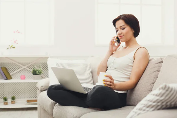 Mädchen mit Laptop und Handy sitzt auf beigem Sofa. — Stockfoto