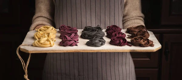 Chef mujer sosteniendo tablero de madera con coloridos nidos fettuccine — Foto de Stock