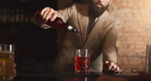 Bartender pouring red liquor to measuring glass