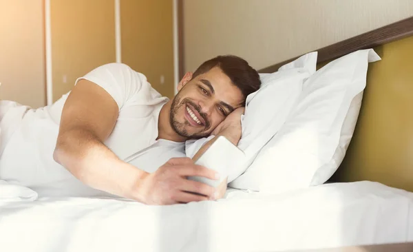 Young man sending message while lying in bed — Stock Photo, Image