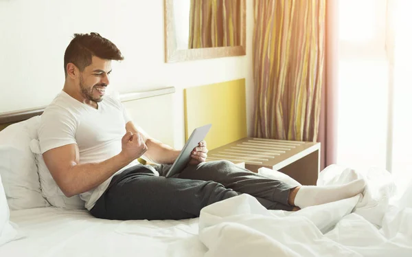 Mladý muž pomocí doigital tabletu, zatímco sedí na posteli — Stock fotografie