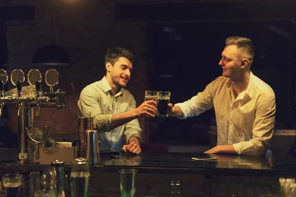 Два счастливых молодых человека разговаривают и пьют пиво в баре — стоковое фото