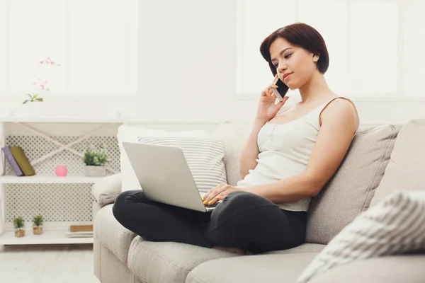 Mädchen mit Laptop und Handy sitzt auf beigem Sofa. — Stockfoto