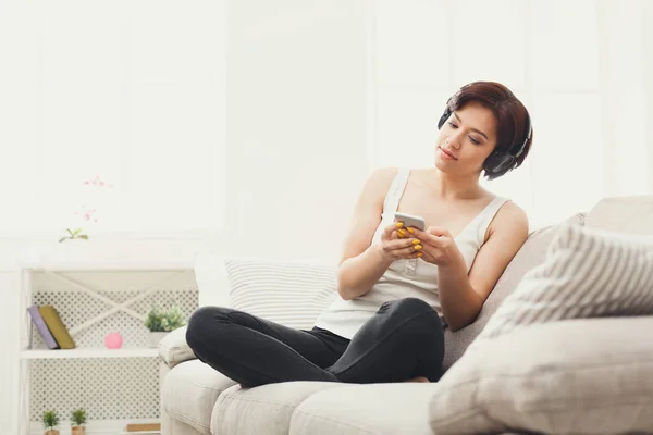 Young woman in headphones on beige couch — Stock Photo, Image