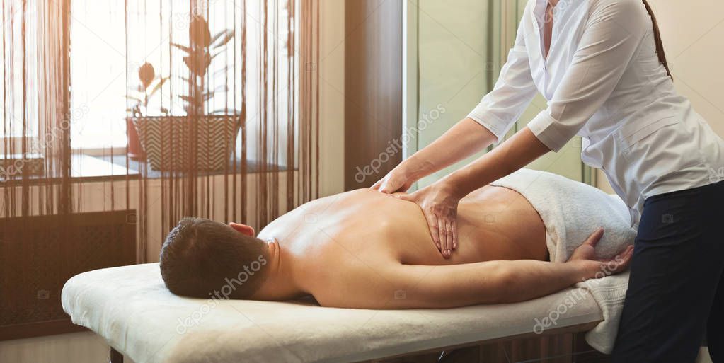 Female massage therapist massaging male back in spa center