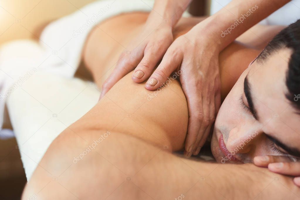 Masseur doing shoulder massage on man body