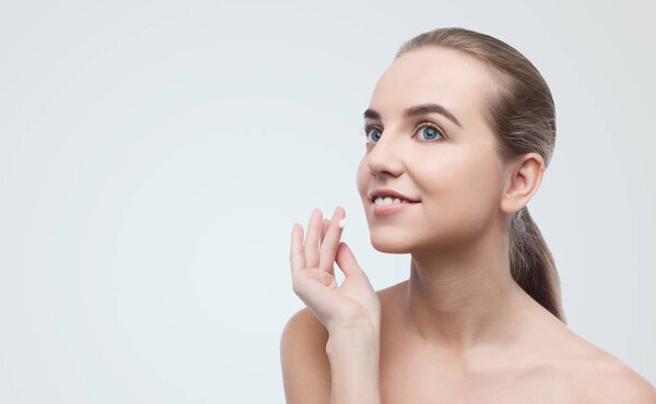 Young woman applying face cream on grey background