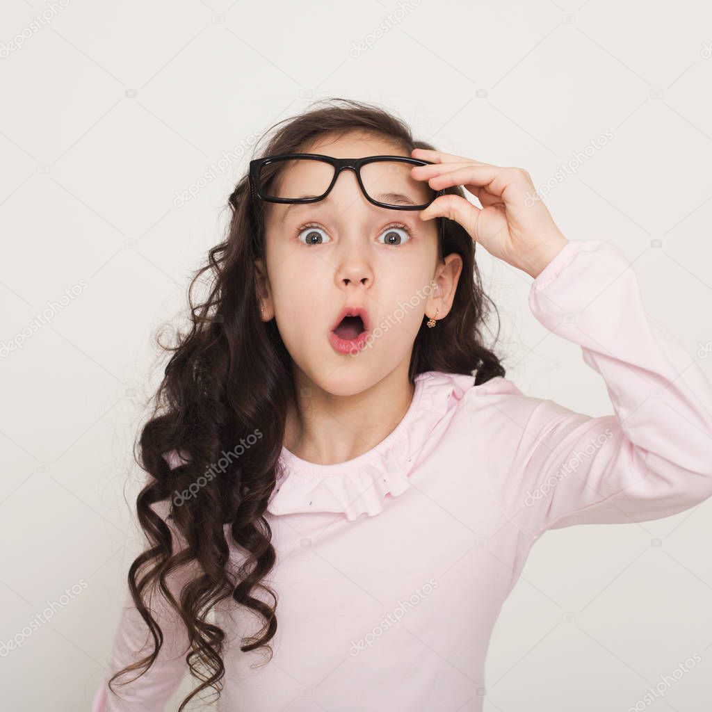 Amazed little girl portrait. Cute child looking surprised, raising glasses in excitement