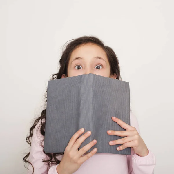 Schockiertes kleines Mädchen bedeckt Gesicht mit Buch. — Stockfoto