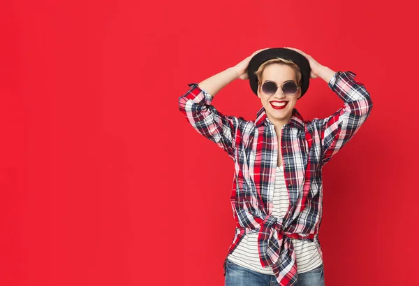 Menina feliz em óculos de sol e chapéu no fundo vermelho — Fotografia de Stock