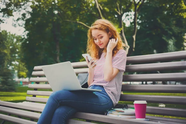 Pelirroja chica usando el teléfono móvil y portátil al aire libre — Foto de Stock