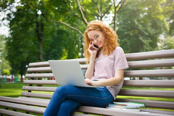 若い赤毛の学生の女の子の携帯電話で呼び出すノート パソコンでの作業 — ストック写真