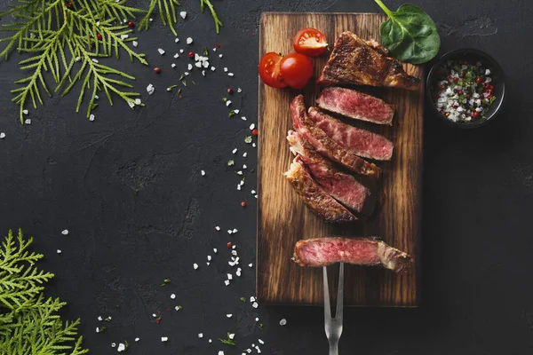 Rib eye steaks and spices on black background — Stock Photo, Image