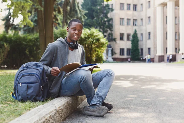 Studente afro-americano seduto con taccuino nel campus universitario — Foto Stock