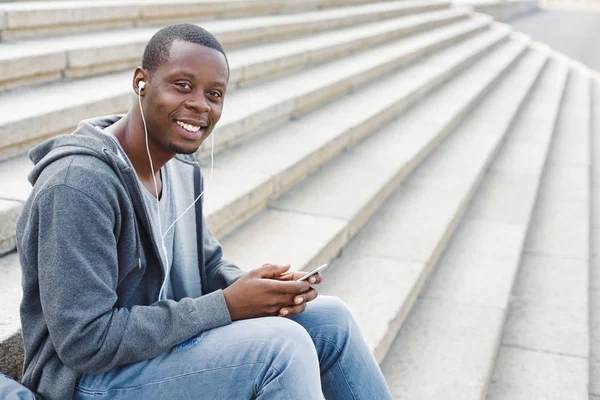 Estudiante afroamericano sentado en las escaleras y usando su smartphone —  Fotos de Stock