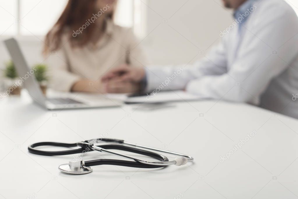 Stethoscope on desk, doctor supporting woman