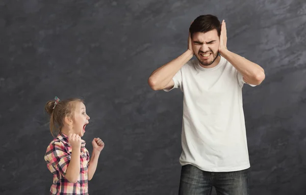 Мужчина закрывает уши, чтобы спрятаться от кричащей маленькой девочки — стоковое фото