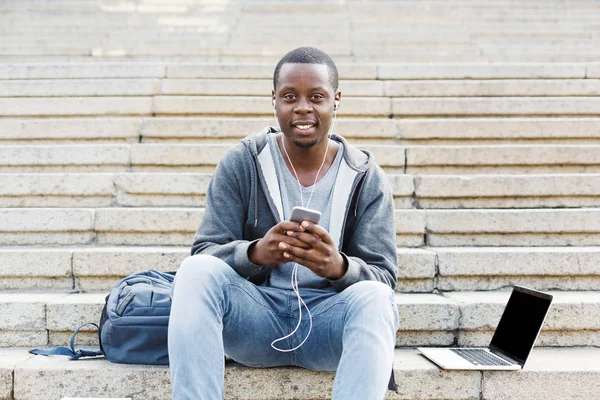 Student afro-american stând pe scări și folosind smartphone-ul său — Fotografie, imagine de stoc