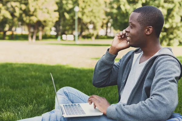 Estudante afro-americano feliz usando laptop no parque — Fotografia de Stock