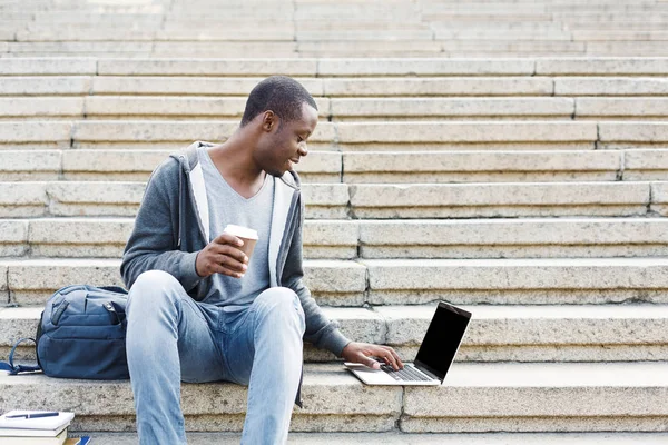 Красивый афроамериканец с ноутбуком и кофе на открытом воздухе — стоковое фото