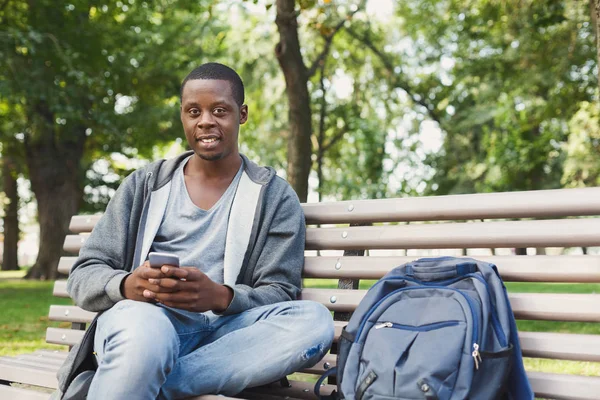 Happy africký student pomocí smartphone venku, usmívající se a sebevědomý — Stock fotografie