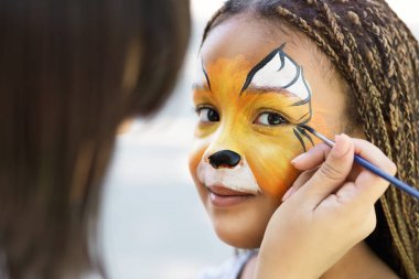 Little girl getting her face painted by face painting artist. clipart