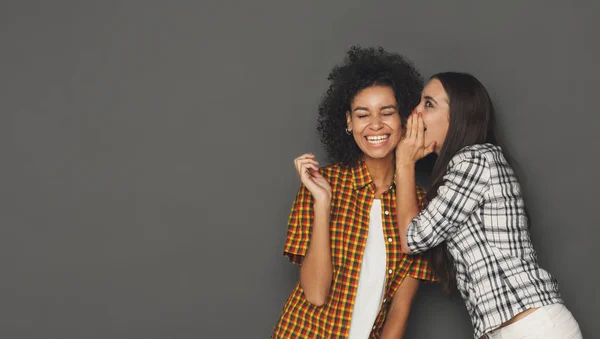 Jonge vrouw naar haar vriend tegen de grijze achtergrond fluisteren — Stockfoto